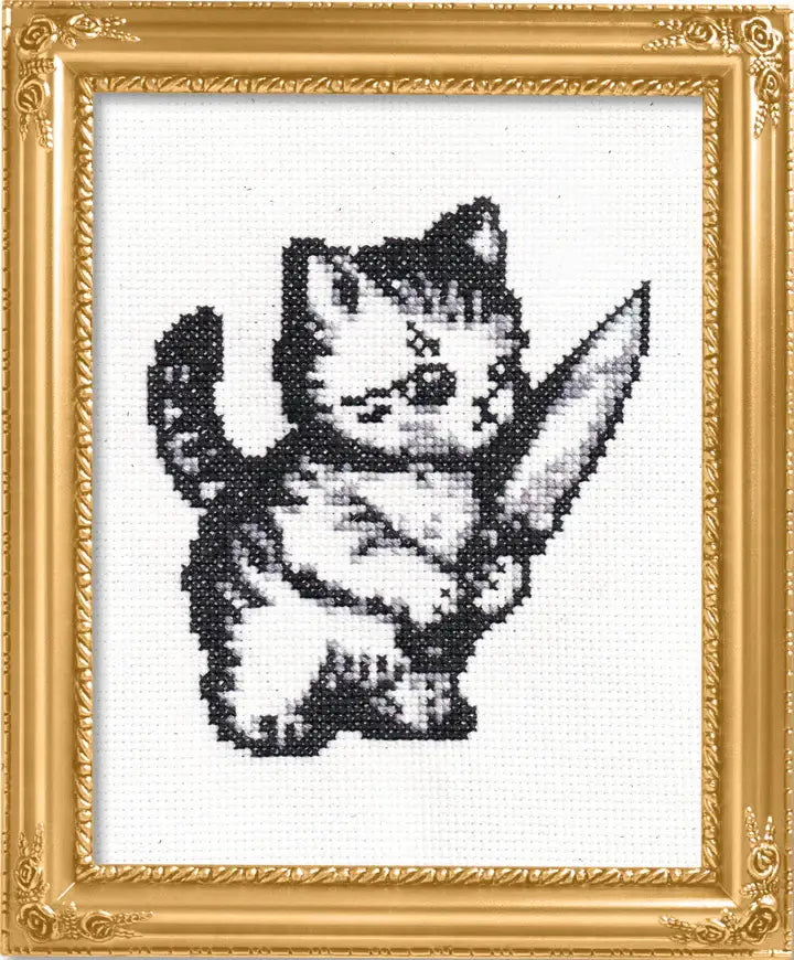 Cross-stitched design of a cat holding a knife in a decorative gold frame.