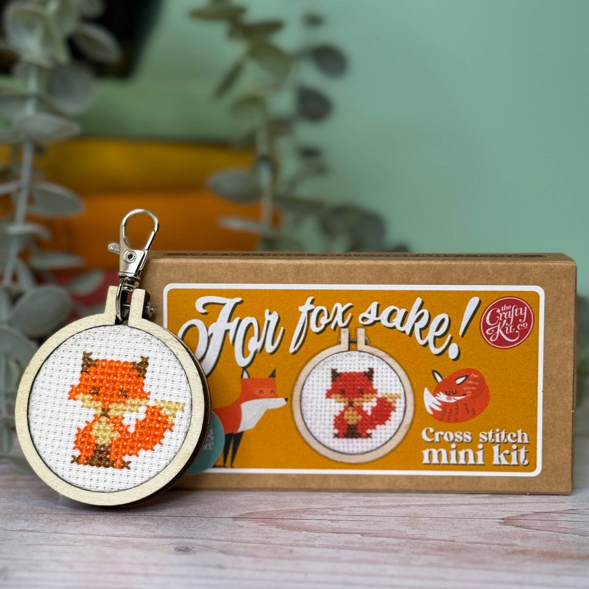 Cross stitch mini kit with fox design and packaging on a wooden surface.
